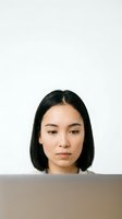 Young woman of East Asian descent with shoulder-length black hair, wearing neutral expression while working on laptop. Isolated on white background for professional and corporate design use.