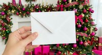 Hand holding white envelope against festive Christmas garland with pink ribbons and twinkling lights for holiday greeting cards and seasonal messaging.