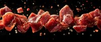 Raw meat cubes flying in motion against black background with spices and herbs scattered around, dramatic food photography for restaurant menu design.