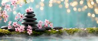 Zen spa stones balanced on moss with pink cherry blossoms and warm bokeh lights creating peaceful meditation atmosphere for wellness and relaxation.