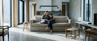 Caucasian mother and child sitting together on a cozy sofa in a modern minimalist living room with large windows and natural light.