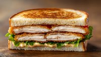 Grilled turkey club sandwich with crispy bacon, fresh lettuce and tomato on toasted bread, perfect for restaurant menus and food advertising campaigns.