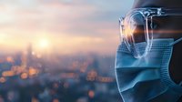 Person wearing protective face mask and glasses against blurred city sunset background with bokeh lights, reflecting pandemic safety measures.