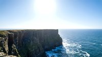 Dramatic coastal cliff formation rising above turquoise ocean waters under clear blue sky, suitable for travel and nature backgrounds.