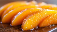 Fresh juicy peach slices arranged in a row on wooden surface, glistening with sweet syrup. Close-up macro shot showing detailed texture and natural fruit pattern.