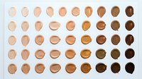 Foundation makeup swatches in diverse skin tone shades arranged in rows on white background, showcasing full spectrum from fair to deep dark.