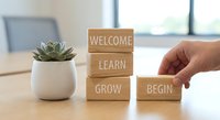 Hand placing wooden blocks with motivational words welcome learn grow begin next to succulent plant on desk for personal development concept.