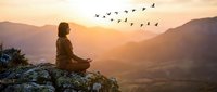 Woman meditating on mountain peak at sunset with birds flying overhead, peaceful mindfulness practice in nature, spiritual wellness and inner peace concept.