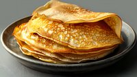 Stack of golden homemade crepes or thin pancakes served on dark ceramic plate against gray background, close up view of traditional breakfast food.