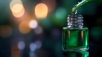 Green essential oil dropping from pipette into glass bottle with warm bokeh lights background for aromatherapy wellness spa and natural skincare products.