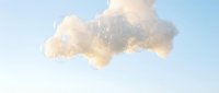Soft fluffy cloud floating in pastel blue sky with warm golden sunlight creating dreamy atmospheric mood for meditation and wellness content.