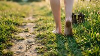 Barefoot person walking on grassy dirt path outdoors, enjoying nature and fresh air during summer season for wellness and lifestyle content.