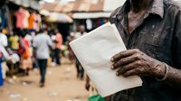 Mature man of African descent holding blank white paper at outdoor market gathering, suitable for community engagement, voting, documentation, or grassroots communication concepts.