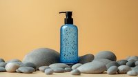 Blue glass pump bottle with water drops on smooth pebbles and stones against warm beige background, spa and wellness concept for cosmetic product packaging.