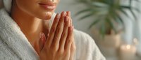 Young woman in white bathrobe with hands in prayer position during meditation or mindfulness practice at home spa with soft lighting and plants.