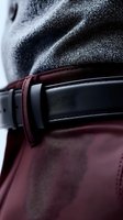 Close-up macro shot of black leather belt on burgundy leather surface with gray textile in background, showing luxury fashion accessories detail and texture.
