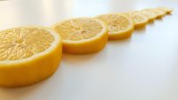 Fresh lemon slices arranged in a row on a white surface, showcasing vibrant yellow citrus fruit in a clean, minimalist food photography style.