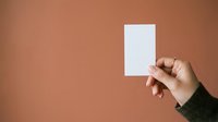 Hand holding blank white card against warm terracotta background, mockup for business cards, invitations, or promotional materials.