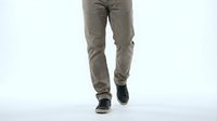 Man walking in beige casual pants and dark sneakers on white background, lower body shot showing confident stride for fashion and lifestyle use.