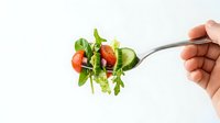Fresh mixed salad greens with cherry tomatoes on fork held by hand against white background for healthy eating and diet concepts.