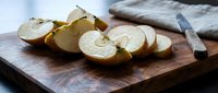 Fresh sliced apples on wooden cutting board with knife, healthy snacking and cooking preparation concept for kitchen and food photography.