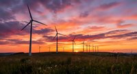 Wind turbines generating renewable energy at sunset with dramatic colorful sky over green field landscape for sustainable power and environmental concepts.