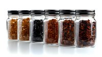 Glass jars filled with various dried spices and herbs arranged in row on white background for culinary cooking and seasoning kitchen storage.
