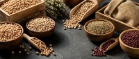 Assorted legumes and grains in wooden bowls and sacks on dark surface, including chickpeas, lentils, and beans for cooking and nutrition.