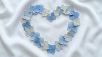 Blue and white paper flowers arranged in heart shape on soft fabric background for romantic wedding decoration and craft projects.
