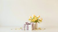 Elegant spring tulip bouquet with gift box and scattered petals on neutral background for Mother's Day, birthday celebrations and romantic occasions.