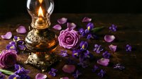 Vintage oil lamp glowing warmly surrounded by purple roses and violet petals on rustic wooden surface creating romantic atmospheric mood.