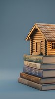 Miniature wooden log cabin model sitting on stack of real estate and architecture books against blue background for education and investment concepts.