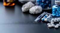 Medical supplies and drugs scattered on dark surface including white pills, blue capsules, syringe and glass bottle, dramatic lighting with copy space.
