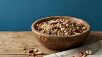 Mixed legumes and beans in rustic wooden bowl on natural linen fabric against blue background for healthy cooking and nutrition concepts.