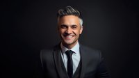 Confident mature Caucasian businessman with gray hair and charming smile wearing dark suit against black background, professional corporate portrait in low key lighting.