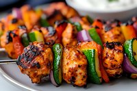 Grilled chicken kebabs with colorful bell peppers, zucchini, and red onions on metal skewers, close-up view showing charred edges and glazed marinade.