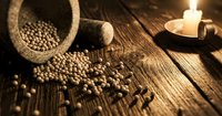 Rustic wooden mortar and pestle with scattered coriander seeds on weathered wood table by candlelight creating warm atmospheric cooking scene.