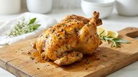 Golden roasted whole chicken with herbs and spices on wooden cutting board, garnished with fresh rosemary and lime wedges for gourmet cooking and dining.