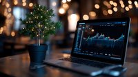 Laptop displaying financial chart with small decorated Christmas tree on desk against blurred bokeh lights background, creating festive business atmosphere.