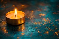 Glowing tea light candle on textured turquoise surface with golden reflections creates atmospheric mood for meditation, spa, or spiritual practices.