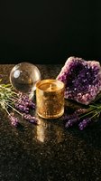 Spiritual wellness setup with amethyst crystal, burning candle, crystal ball and lavender herbs on dark surface for meditation and healing practices.