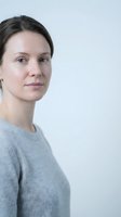 Natural portrait of confident middle-aged Caucasian woman in gray sweater looking at camera with gentle smile against neutral background for lifestyle content.