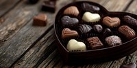 Assorted chocolate pralines in heart-shaped box on rustic wooden table, perfect for Valentine's Day, anniversary, or romantic gift.