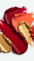Colorful lipstick smears in red orange and gold tones creating artistic makeup swatches on white background for cosmetic and beauty product advertising.