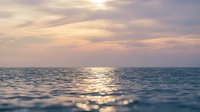 Serene ocean seascape at sunset with golden sunlight reflecting on calm water waves, ideal for travel, wellness, and nature-themed designs.