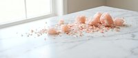 Pink Himalayan salt crystals scattered on white marble surface in bright natural light for cooking and wellness applications.