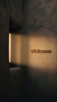 Welcome sign on a textured concrete wall illuminated by warm light streaming through a narrow window in a moody interior.