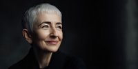 Portrait of senior woman with short white hair and warm smile against dark background, showcasing confidence and wisdom in elegant black attire.