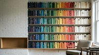 Colorful rainbow bookshelf with organized books by color creating vibrant home library display against white brick wall for interior design inspiration.