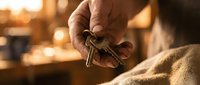 Elderly man's weathered hands holding house keys in warm golden light, symbolizing homeownership, real estate investment, and property security.